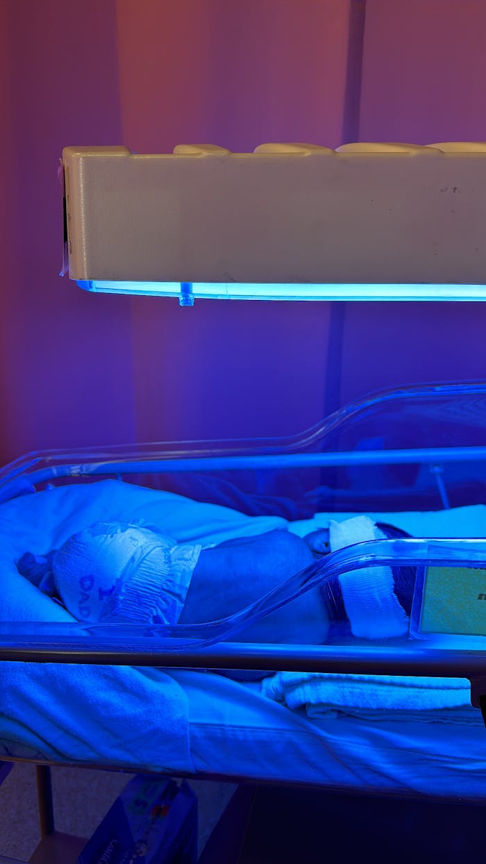 A newborn baby receiving phototherapy treatment in an incubator under blue light.